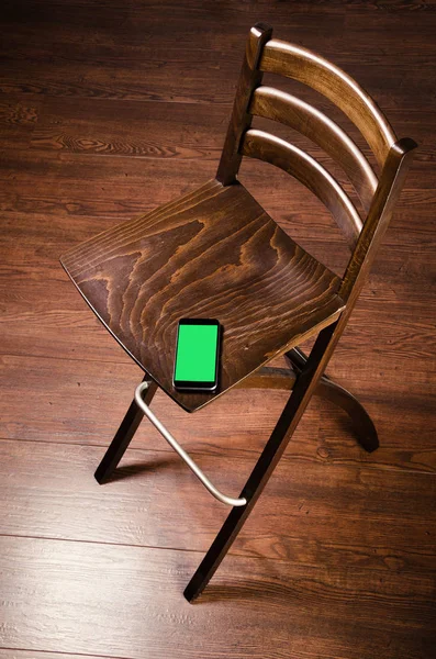 Wooden chair and phone. Designer furniture. Mobile phone with green screen.  Beautiful brown chair on the hardwood floor.