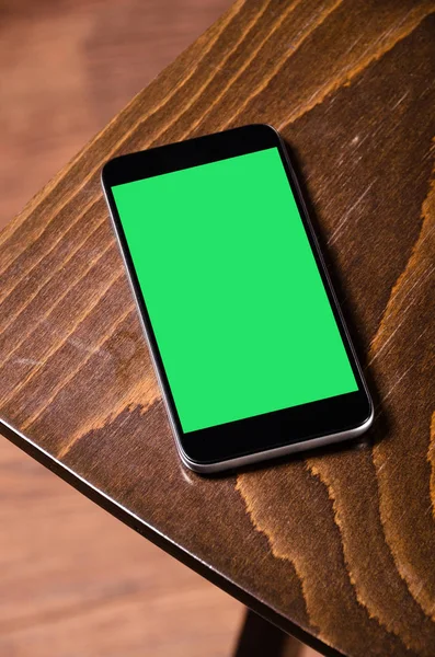 Wooden chair and phone. Designer furniture. Mobile phone with green screen.  Beautiful brown chair on the hardwood floor.