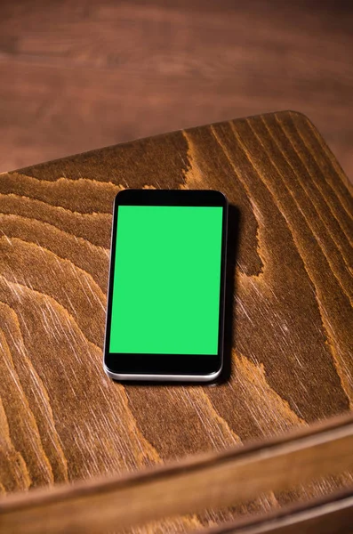 Wooden chair and phone. Mobile phone with green screen.