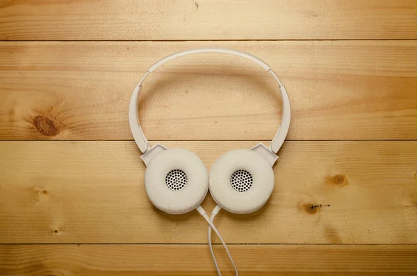 White headphones on wooden table. Modern headphone with cable.