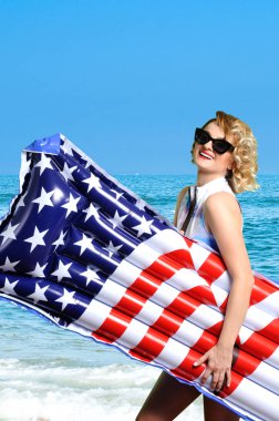 Yaz tatili. Güneş kadın bikini ile şişme yatak Amerikan bayrağı sahilde zevk.