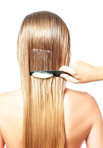 Hair care. Woman with comb is applying hair conditioner on her wet blonde hair