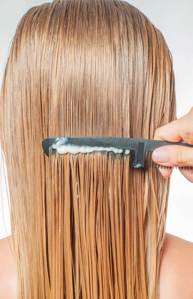 Hair care. Woman with comb is applying hair conditioner on her wet blonde hair