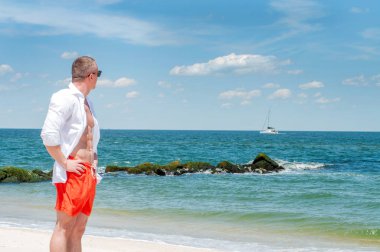 Şort ve beyaz gömlek güzel sahilde duran yakışıklı adam 