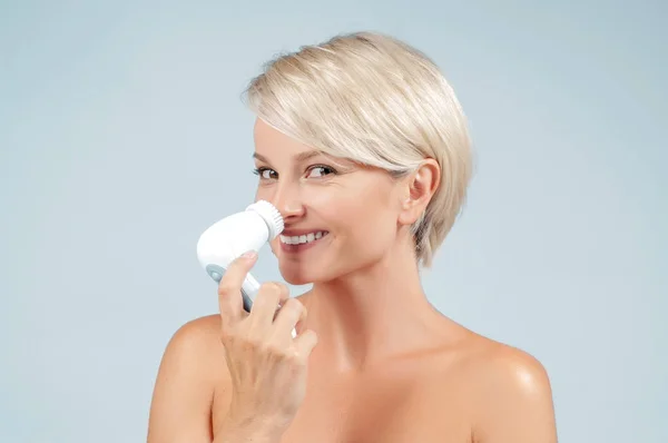 Happy woman cleaning face skin with brush and foam. Natural cosmetic. Facial beauty treatment concept.