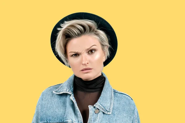 Negative emotions. Angry girl expressing anger. Displeased young woman frowning eyebrows looking at camera on yellow background