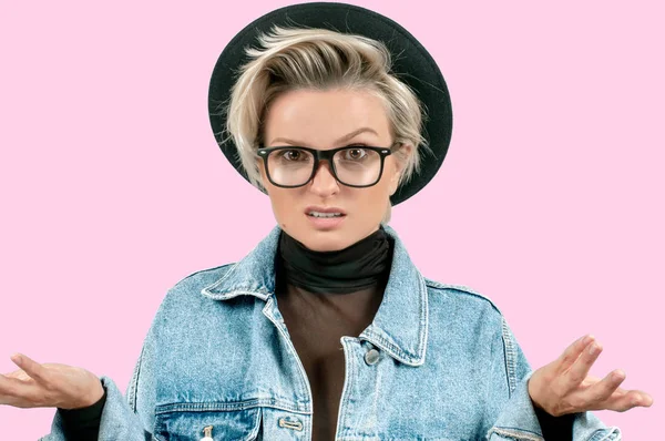 Negative human emotions. Angry girl expressing anger. Woman in fashionable hat and glasses with displeased face expression on pink background