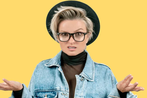 Negative human emotions. Angry girl expressing anger. Woman in fashionable hat and glasses with displeased face expression on yellow background