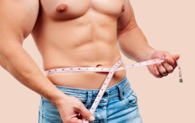 Kusursuz bir beden beline pastel arka plan üzerinde ölçüm ile kas adam.