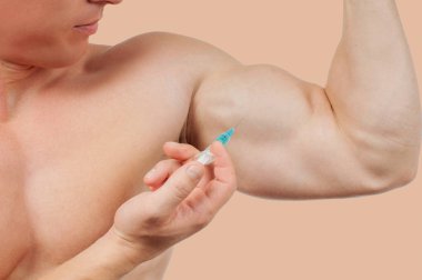 Steroid enjeksiyonu pastel arka plan koluna alarak vücut geliştirmeci. 