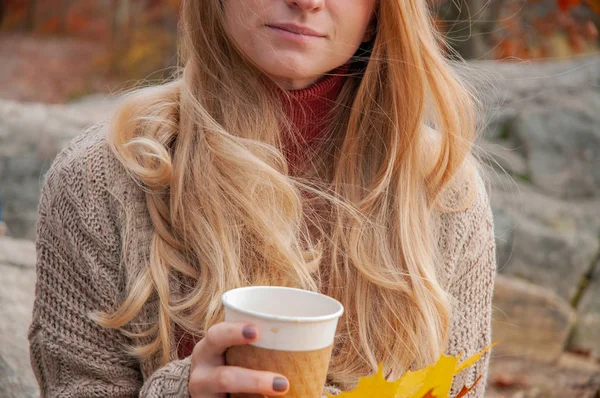 Woman holding cup of coffee in the hands outdoor. Beautiful woman drinking coffee in autumn park.