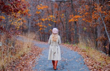 Sonbahar paltolu güzel kadın sonbahar ormanda yürüyor.