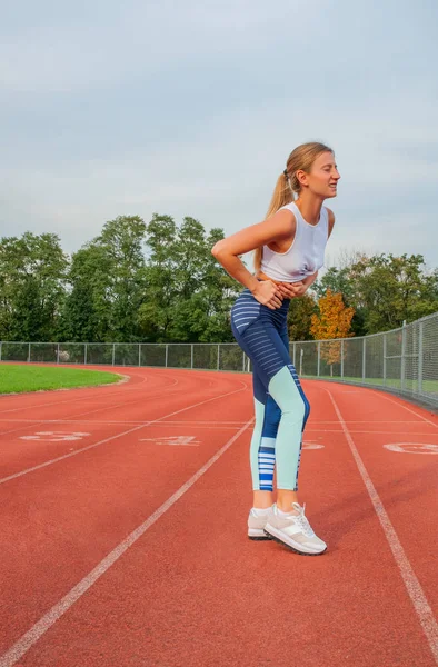 Athletic woman on running track has side cramps during workout