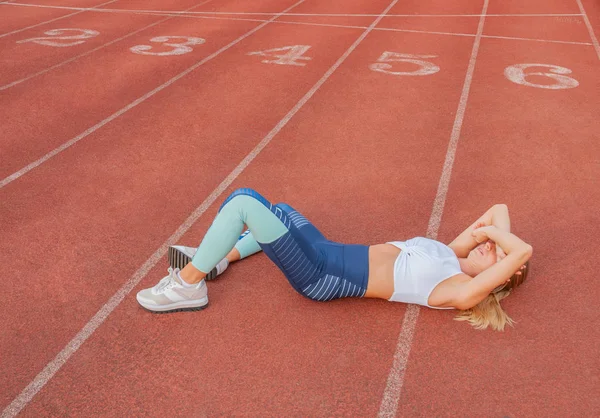 Tired woman runner taking a rest after run lying on the running track