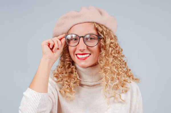 暖かいセーター ベレー帽 灰色の背景にカメラを見て眼鏡を着た巻き毛を持つ学生の女性の肖像画 — ストック写真