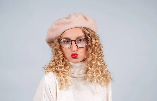 暖かいセーター ベレー帽 灰色の背景にカメラを見て眼鏡を着た巻き毛を持つ学生の女性の肖像画 — ストック写真