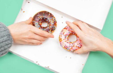 Kadın elleri pastel yeşil arka planda kutuda iki son donut alıyor. 