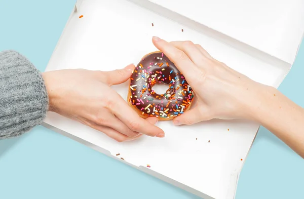 Female hands is taking last donuts in box on pastel blue background.