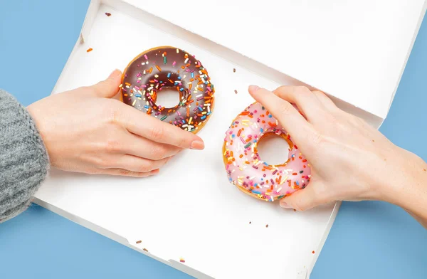 Frauenhände nehmen zwei letzte Donuts in Schachtel auf pastellblauem Hintergrund. — Stockfoto