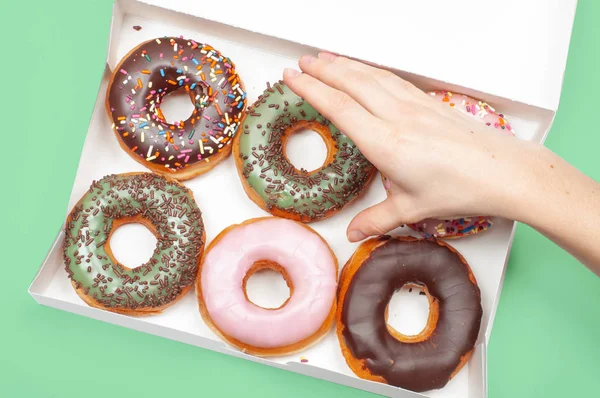 Frauenhände nehmen Donuts in Schachtel auf pastellgrünem Hintergrund entgegen — Stockfoto