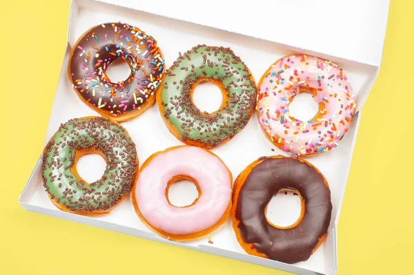 Colorful donuts in box on yellow background