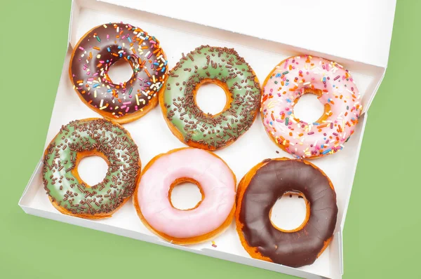 Donuts coloridos en caja sobre fondo verde —  Fotos de Stock
