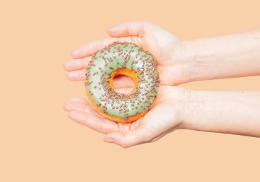Pastel arka planda renkli donut tutan kadın elleri