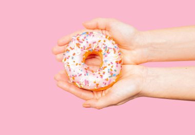 Pastel pembe arka planda renkli donut tutan kadın eller