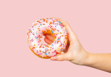 Pastel pembe arka planda renkli donut tutan kadın el