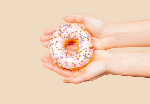 Weibliche Hände mit buntem Donut auf pastellfarbenem Hintergrund — Stockfoto