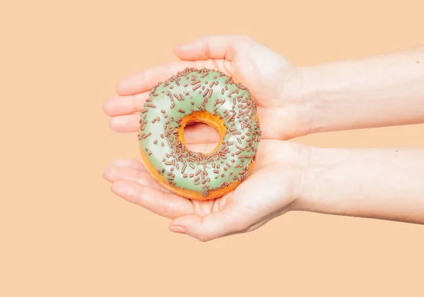 Manos femeninas sosteniendo rosquilla colorida sobre fondo pastel — Foto de Stock