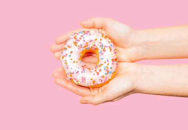 Weibliche Hände mit buntem Donut auf pastellrosa Hintergrund — Stockfoto