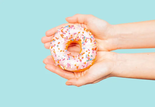 Weibliche Hände mit buntem Donut auf pastellblauem Hintergrund — Stockfoto