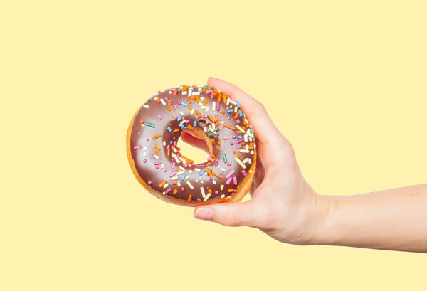 Mão feminina segurando donut colorido no fundo amarelo pastel — Fotografia de Stock