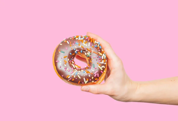 Mão feminina segurando donut colorido no fundo rosa pastel — Fotografia de Stock