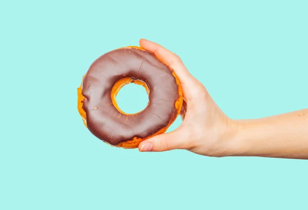 Mão feminina segurando donut colorido no fundo azul pastel — Fotografia de Stock