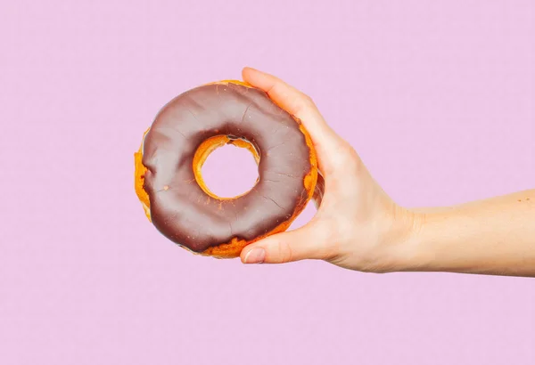 Mão feminina segurando donut colorido no fundo rosa pastel — Fotografia de Stock