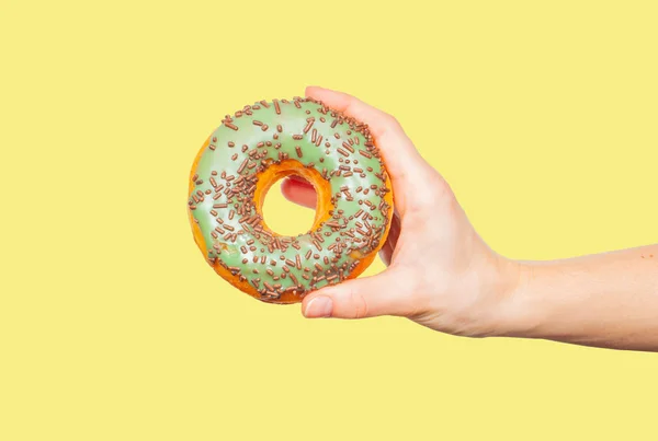 Mão feminina segurando donut colorido no fundo amarelo pastel — Fotografia de Stock