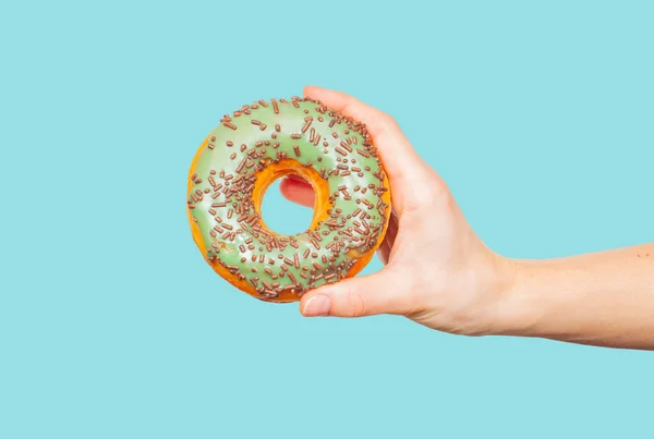 Mão feminina segurando donut colorido no fundo azul pastel — Fotografia de Stock