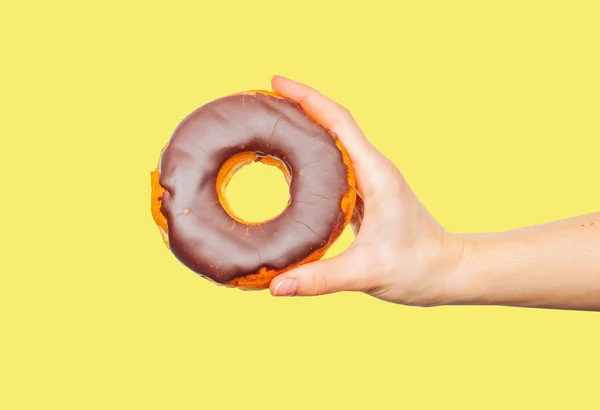 Mão feminina segurando donut colorido no fundo amarelo pastel — Fotografia de Stock