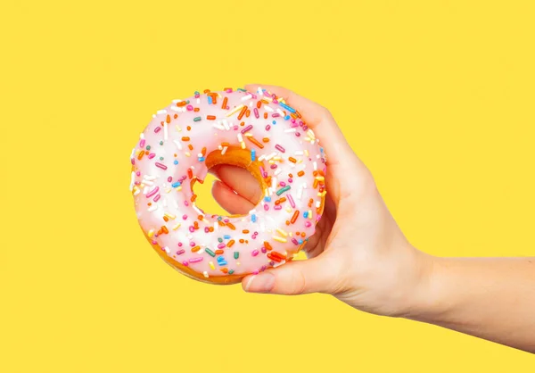 Weibliche Hand hält bunten Donut auf pastellgelbem Hintergrund — Stockfoto