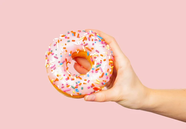 Mano femenina sosteniendo rosquilla colorida sobre fondo rosa pastel —  Fotos de Stock