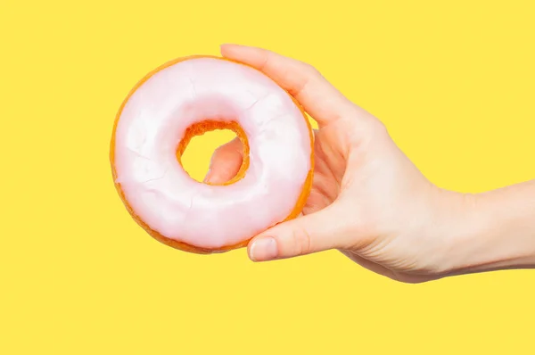 Mão feminina segurando donut colorido no fundo amarelo pastel — Fotografia de Stock