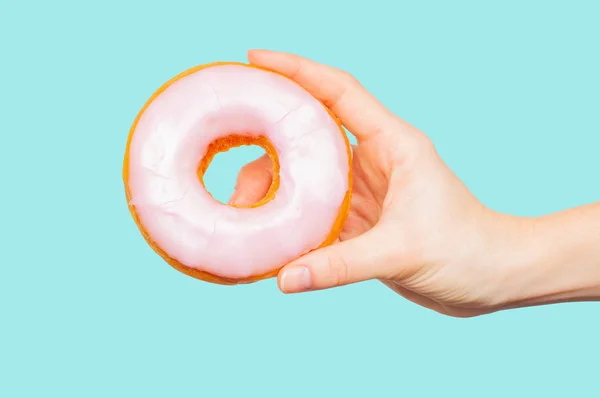 Weibliche Hand hält bunten Donut auf pastellblauem Hintergrund — Stockfoto