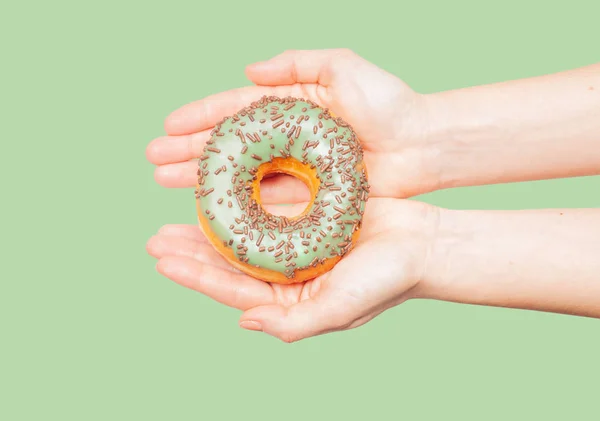 Weibliche Hände mit buntem Donut auf pastellgrünem Hintergrund — Stockfoto