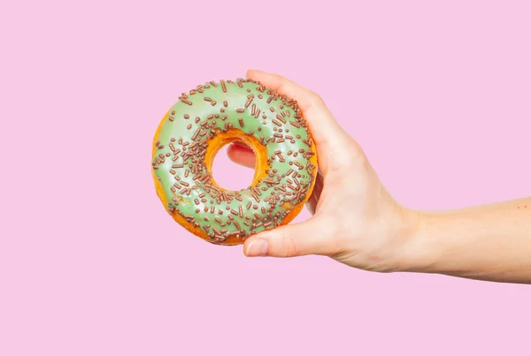 Mão feminina segurando donut colorido no fundo rosa pastel — Fotografia de Stock