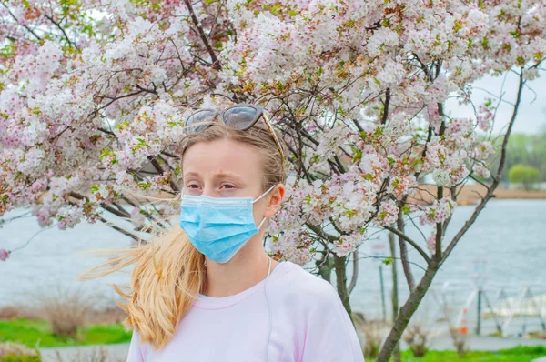 Alergia. Mujer joven en máscara protectora de la alergia al polen, entre los árboles en flor en el parque . —  Fotos de Stock