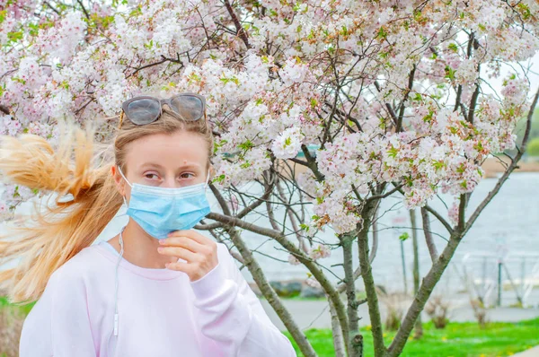 Alergia. Mulher nova na máscara protetora da alergia do pólen, entre árvores florescendo no parque . — Fotografia de Stock