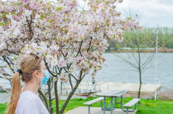 Allergy. Young woman in protective mask from pollen allergy, among blooming trees in park. — Stock Photo, Image