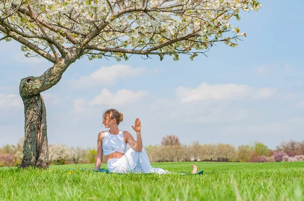 Femeia practică yoga, făcând Ardha Matsyendrasana să pozeze lângă copacul înflorit — Fotografie, imagine de stoc